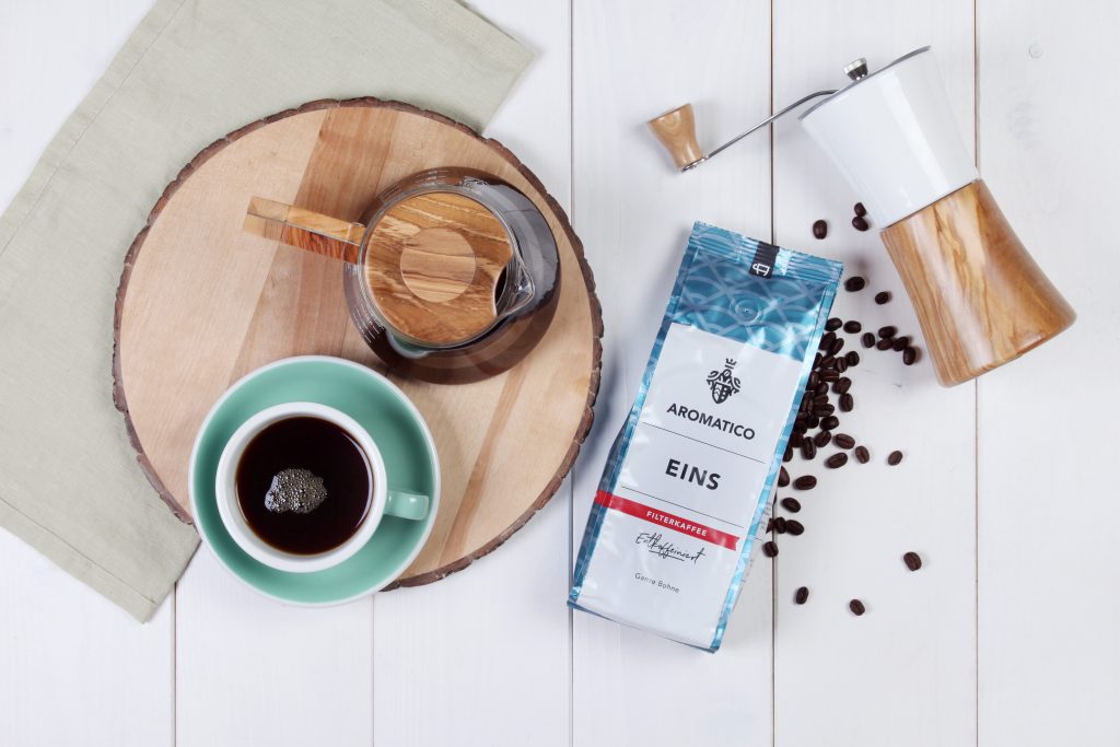 Der Aromatico Eins Kaffeepackung neben Kaffeemühle und Tasse