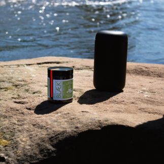 Blaek Kaffee und Thermobecher auf einem Stein im Hintergrund ist Wasser zu sehen