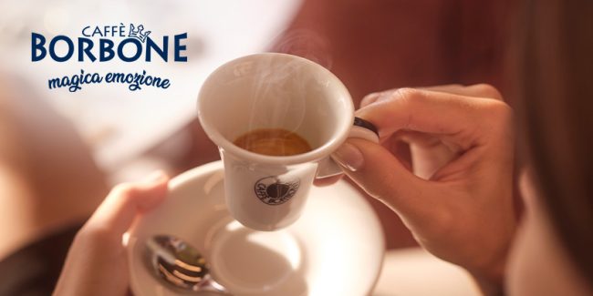 Person hält weiße Espressotasse gefüllt mit Kaffee in der Hand