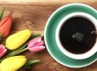 Türkise Kaffeetasse auf Holzuntergrund, daneben Tulpen in verschiedenen Farben