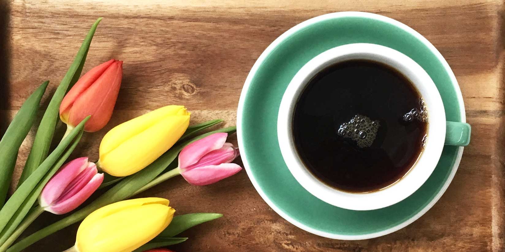 Türkise Kaffeetasse auf Holzuntergrund, daneben Tulpen in verschiedenen Farben