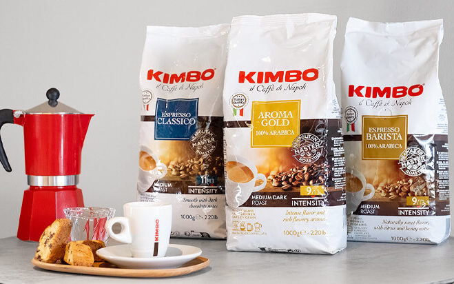 Kimbo Espresso Kaffeeverpackungen auf einem runden Tisch. Daneben ein roter Espressokocher und weiße Espressotasse.