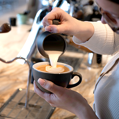 Essse Selezione Speciale als Cappuccino Aufgeschäumte Milch wird mit einem Milchkännchen auf den Espresso in der Cappuccinotasse gegossen.