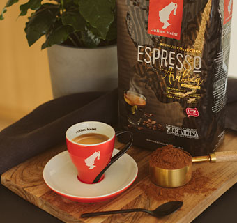 Rote Julius Meinl Espressotasse auf Holztisch mit einer Espressotüte und Kaffeemehl
