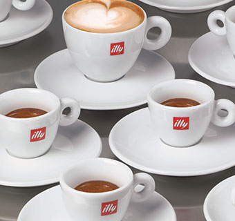 drei illy Espressotassen gefüllt mit Espresso und ein Cappuccino mit Latte Art Herz